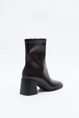 Bota corta de caña elástica, color negro con acabado charolado. Presenta puntera cuadrada y taco medio geométrico y ancho.