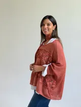 Sweater de punto color naranja con diseño holgado, que incorpora franjas horizontales de encaje con motivos florales. Presenta mangas tres cuartos con puños abotonados y se complementa con una bufanda del mismo tejido y color.