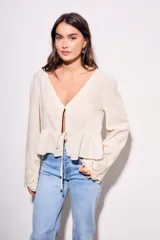Blusa beige de viscosa y lino, con escote en V, mangas largas acampanadas con detalles bordados tipo broderie, y cierre frontal con lazo para anudar.