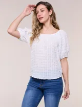 Blusa blanca de tela texturada y silueta fluida, con escote en U y frunces. Cuenta con mangas cortas abullonadas con elástico en los puños y ruedo redondeado.
