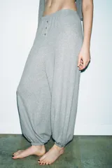 Pantalón de tiro alto confeccionado en tejido de punto mezcla de algodón, con cintura elástica y detalle de botones frontales. Presenta un diseño de pernera amplia con bajo abullonado acabado en elástico.