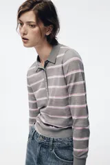Polo de punto fino confeccionado en lana, con diseño de rayas horizontales en tonos gris, blanco y rosado. Presenta cuello polo, manga larga y cierre frontal con botones.