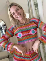 Top corto de crochet multicolor con diseño de rayas horizontales y mangas largas acampanadas. Presenta detalles de flores aplicadas en la zona del pecho.