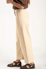 Pantalón de corte baggy y tiro medio, confeccionado en algodón peinado de color arena. Presenta diseño de pierna ancha, cierre frontal con botón y bolsillos laterales.