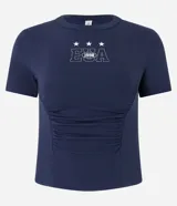 Blusa baby look azul marino de algodón, con cuello redondo, manga corta, drapeado delantero y estampa lettering "EUA" con estrellas.