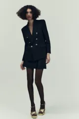 Blazer de corte entallado con cuello y solapa, manga larga y hombros marcados. Presenta un cierre frontal cruzado con botones dorados y bolsillos delanteros con solapa.