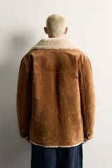 Campera marrón de piel con interior de borreguillo color crudo, de corte regular fit, con cuello bowling, bolsillos de doble vivo y cierre frontal con botones.