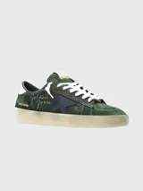 Zapatillas Golden Goose modelo Stardan, confeccionadas en gamuza color verde oscuro con detalles en cuero nappa. Presentan la icónica estrella lateral en azul marino, firma de la marca bordada en el lateral y suela con efecto desgastado.