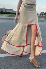 Falda midi color beige confeccionada en lino, con corte irregular, volados y ribete rojo.