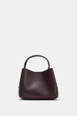 Bolso tipo saca de color bordó, con asa de mano trenzada y cierre mediante botón imantado. Incluye bolsillo interior con cremallera.