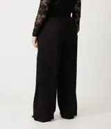 Pantalón negro de vestir, tiro alto, corte wide leg (pierna ancha), con bolsillos laterales y cierre frontal con cremallera y gancho.