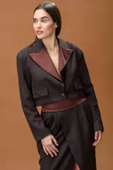 Blazer cropped de color marrón oscuro con solapas en contraste de tono bordó. Presenta un diseño estructurado con cierre frontal de un botón y bolsillos laterales decorativos.