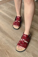 Sandalias planas color rojo cereza, estilo gladiador con tiras anchas y múltiples hebillas metálicas circulares. Cuentan con plantilla anatómica y suela antideslizante.