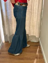 Jean de denim azul con bolsillos delanteros aplicados, costuras verticales y diseño de tablas en los laterales de las piernas amplias.