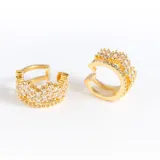 Par de aros ear cuff dorados con cristales claros y diseño de corona. Confeccionados en acero con baño de oro de 18k.