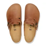 Zueco tipo mule de cuero color cognac, con tira ajustable sobre el empeine y hebilla metálica. Presenta plantilla de corcho y suela de goma antideslizante.