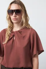 Top negro de manga corta con detalle de nudo en el escote y abertura tipo gota. Presenta una silueta relajada y textura sutil en la tela.