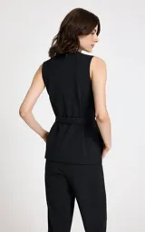 Chaleco sastrero de corte entallado con diseño de raya diplomática vertical. Presenta cuello redondo, sisas sin mangas, detalle cruzado asimétrico en el frente, botones decorativos en el hombro izquierdo y cinturón de tela a juego con hebilla metálica.