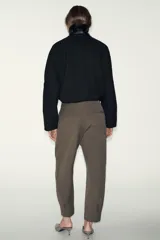 Pantalón de tiro medio con pinzas delanteras, bolsillos laterales y falsos bolsillos de vivo en la parte trasera. Presenta un corte holgado que se estrecha hacia el tobillo, con bajo acabado en pliegues y cierre frontal con cremallera, botón interior y gancho.