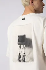 Remera oversize de algodón 100% premium, color blanco hueso, con bordado frontal "90's" en negro y un parche trasero con una imagen estilo videoclip de Nirvana.