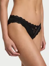 Bombacha estilo bikini de tiro medio color negro, con detalles de encaje en los bordes y aplique floral en el centro.