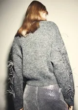 Jersey de punto gris con cuello redondo y adorno de plumas de avestruz en el pecho y las mangas, de corte recto y manga larga.