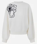 Buzo de algodón color blanco, con diseño de bordado en cuerda negra formando el contorno de una flor en el hombro derecho. Presenta mangas largas con puños ajustados y acabados canelados en cuello y ruedo.