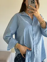 Camisa celeste de corte holgado, con cuello clásico, cierre frontal con botones, bolsillo en el pecho y mangas largas con puños abotonados.