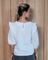 Blusa blanca de algodón tussor, con cuello redondo, mangas 3/4 abullonadas y detalle de volados en los hombros.