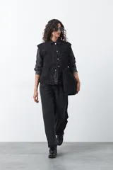 Chaleco de jean negro con corte recto, cierre frontal con botones metálicos y costuras visibles. Presenta un diseño clásico de denim con cuello camisero y hombreras marcadas.