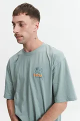 Remera de manga corta color crema, corte oversize, con cuello redondo y estampado con texto y diseño floral en el frente.