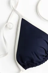 Top de bikini triangular con relleno extraíble, de color azul marino con ribetes blancos y tiras ajustables para atar en la espalda.