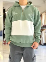 Hoodie de media cierre y capucha, con diseño en bloques de color verde y blanco, con bordados decorativos en el pecho.