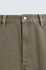 Pantalón de denim color verde oliva, estilo chino con corte ancho y bota acampanada (flare) desde la rodilla. Tiro medio, confeccionado en tejido rígido. Presenta bolsillos frontales y bolsillos traseros de plastrón.