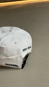 Gorra negra con bordado de las iniciales BG en el frente y diseño de costuras geométricas en la visera.