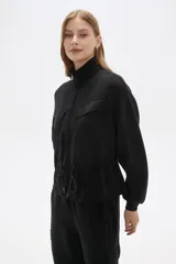 Campera negra de manga larga con cierre frontal, bolsillos frontales con solapa y cordón ajustable en la cintura.