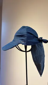 Gorro tipo pañuelo con visera rígida azul marino, confeccionado en lino con estampado de rayas grises y blancas. Presenta un diseño envolvente con caída trasera y detalle de logo bordado en el lateral.