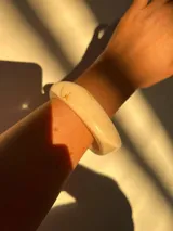 Brazalete rígido de acrílico color crema con vetas marrones.