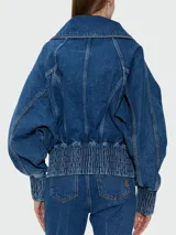 Campera de jean Balmain con cierre frontal, cuello alto y puños elásticos fruncidos. Presenta un diseño estructurado con hombros caídos y bolsillos laterales.