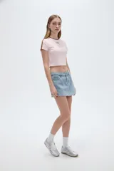 Short pollera de denim celeste claro, de tiro alto y corte mini, con diseño de falda cruzada al frente y detalle de ojales metálicos decorativos en el ruedo.