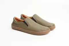 Zapatillas tipo slip-on de gamuza color beige, con diseño barefoot y suela de corcho texturizado. Presenta elásticos laterales negros para un calce fácil.