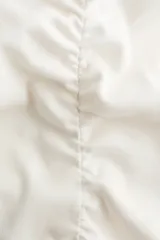 Top de algodón color blanco, con manga japonesa, escote en V delantero y trasero, corte ajustado, ribetes con terminación ondulada y costuras fruncidas en el centro que generan un efecto drapeado.