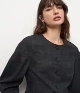 Blazer de sastrería color gris con estampado de cuadros, cuello redondo y cierre frontal con botones forrados. Presenta mangas largas con volumen tipo baloné y bolsillos frontales con solapa.
