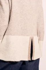 Sweater de punto con cuello alto, corte holgado y diseño color block en tonos beige y blanco.