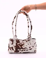 Cartera tipo baguette confeccionada en cuero vacuno con estampado animal print tipo vaca. Cuenta con doble asa de hombro, cierre superior y broches laterales para ajustar su forma.