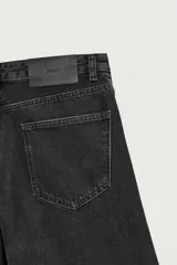 Jeans de denim de algodón en color negro con efecto lavado, corte amplio y silueta curva tipo barrel fit con pinzas en las rodillas. Presenta diseño clásico de cinco bolsillos y cierre frontal con cremallera y botón metálico.