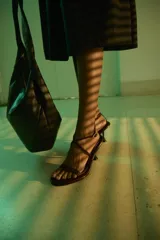 Sandalias negras de cuero vacuno satinado con tiras finas en la capellada, pulsera cruzada al tobillo con hebilla metálica dorada y taco fino de 7,5 cm.