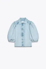 Camisa de denim celeste con cuello solapa, manga corta abullonada y cierre frontal con botones.
