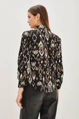 Camisa de manga larga con cuello camisero y cierre frontal de botones. Presenta un estampado étnico tipo ikat en tonos negro, blanco y ocre.