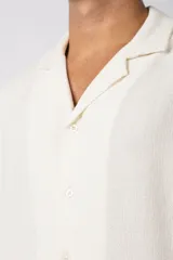 Camisa de manga corta con cuello cubano, confeccionada en lino entramado de textura natural. Presenta un corte relajado y cierre frontal con botones.